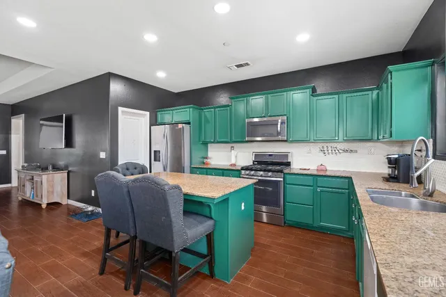 a kitchen with kitchen island granite countertop a sink a stove a refrigerator cabinets and a dining table