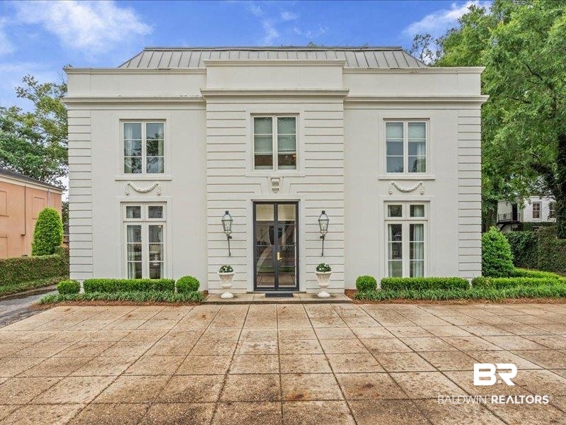 109 Eaton Square Mobile, AL 36608 - Photo 22 of 26 Classical revival façade featuring a central glass entry door, symmetrical windows, and a structured landscape with manicured hedges and topiary