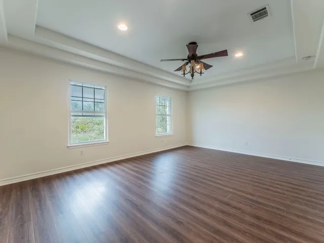 an empty room with wooden floor chandelier fan and windows