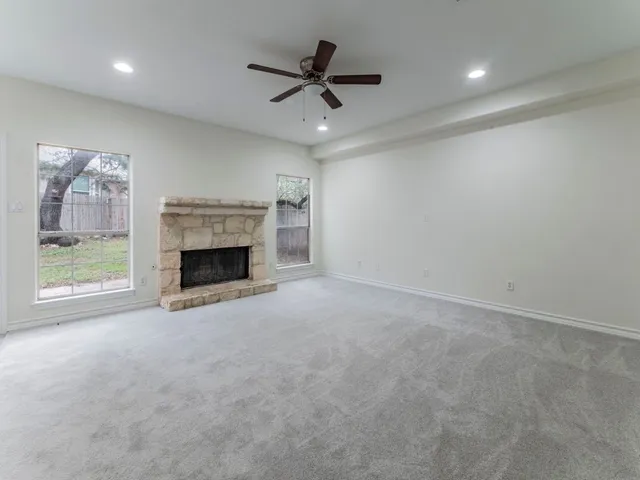 an empty room with windows fireplace and a ceiling fan