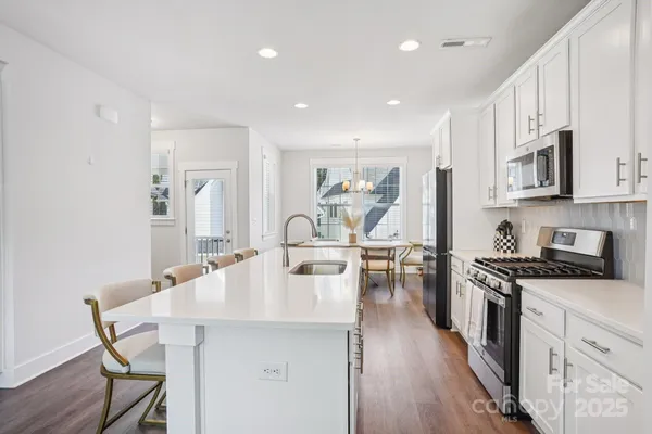 a kitchen with stainless steel appliances kitchen island granite countertop a stove a sink a refrigerator white cabinets and wooden floor