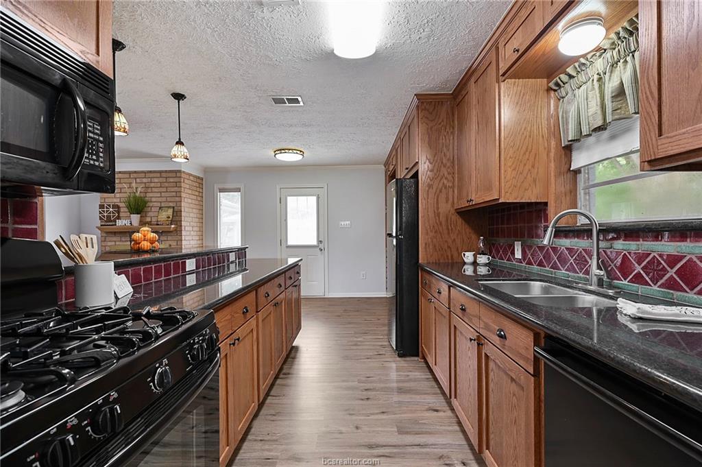 1031 Rose Circle College Station, TX 77840 - Photo 11 of 26 Kitchen with black appliances, tasteful backsplash, dark stone countertops, healthy amount of natural light, and a textured ceiling