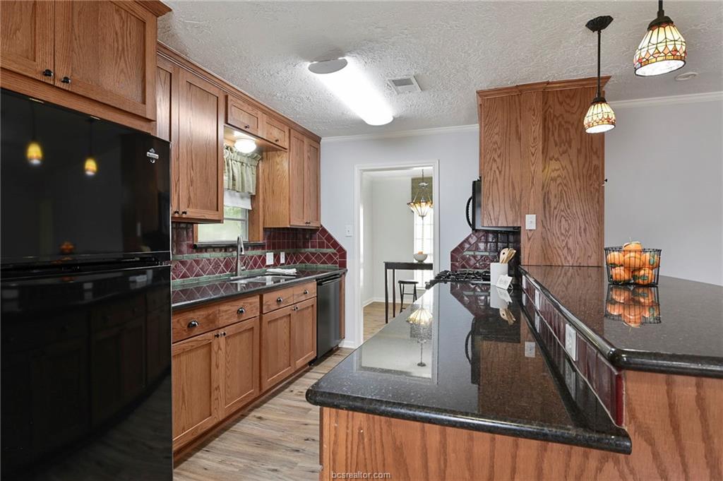 1031 Rose Circle College Station, TX 77840 - Photo 12 of 26 Kitchen with brown cabinetry, freestanding refrigerator, a textured ceiling, light wood-style floors, and dark stone countertops