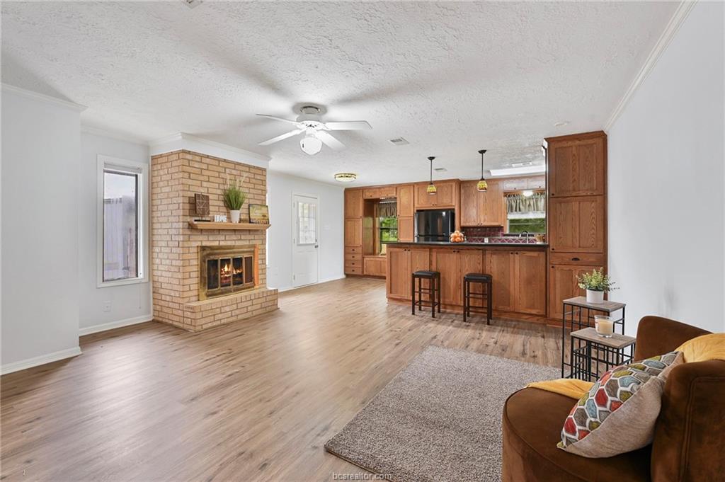 1031 Rose Circle College Station, TX 77840 - Photo 2 of 26 Living room featuring light wood finished floors, a textured ceiling, ceiling fan, crown molding, and a fireplace