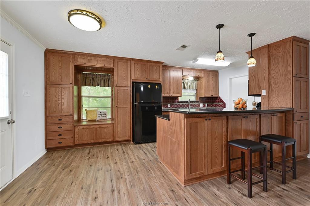1031 Rose Circle College Station, TX 77840 - Photo 9 of 26 Kitchen featuring brown cabinetry, a peninsula, light wood-style flooring, freestanding refrigerator, and a textured ceiling
