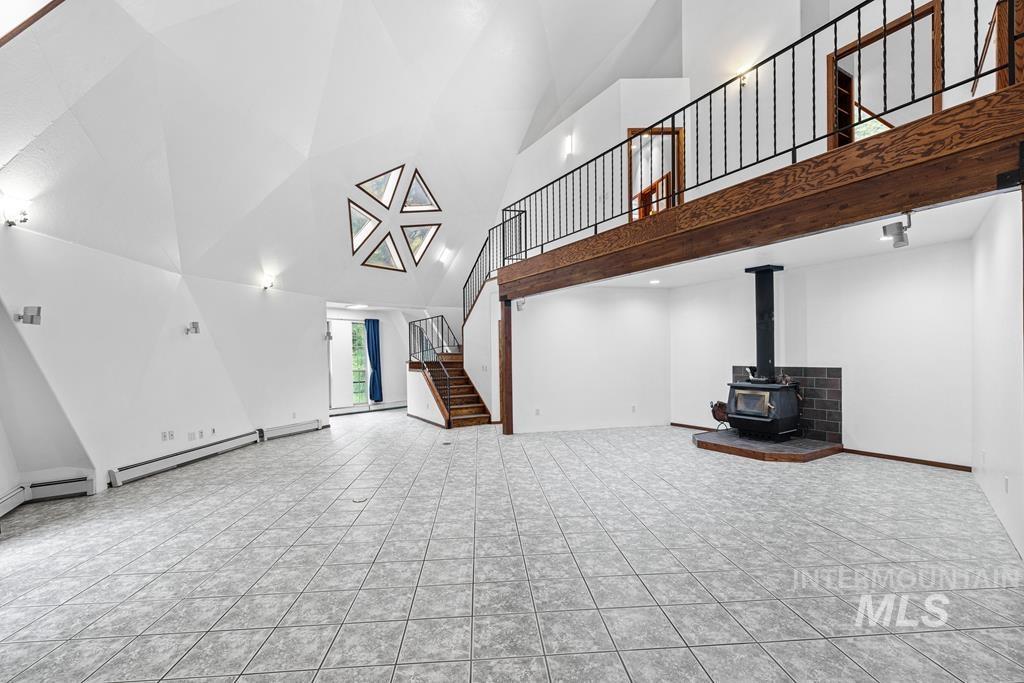 360 Lake Creek Riggins, ID 83549 - Photo 4 of 50 Unfurnished living room featuring a wood stove, a baseboard radiator, vaulted ceiling, and light tile patterned flooring