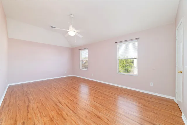 an empty room with wooden floor ceiling fan and windows