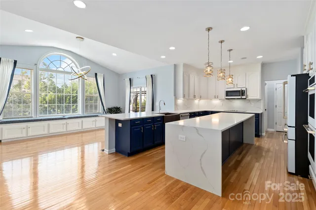 a large kitchen with a large counter top a refrigerator a sink stainless steel appliances and cabinets