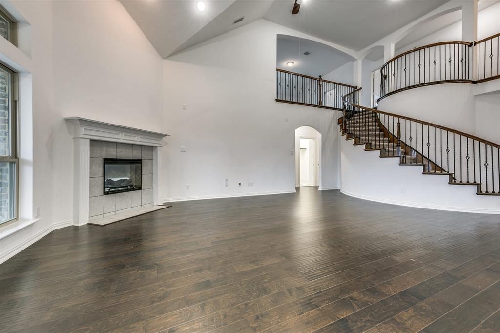 104 Sweetleaf Drive Red Oak, TX 75154 - Photo 9 of 36 Expansive living area featuring dark wood flooring, a fireplace with a light-colored tile surround and mantel, and a grand curved staircase with dark wood handrails and wrought iron balusters