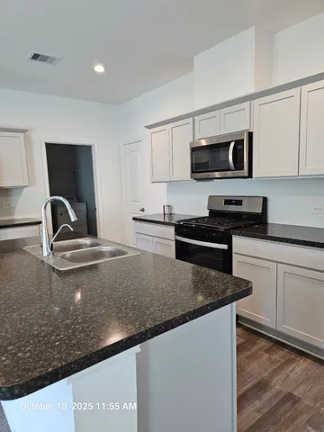 a kitchen with stainless steel appliances a sink dishwasher a stove top oven a refrigerator with white cabinets and wooden floor