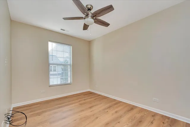an empty room with wooden floor fan and windows