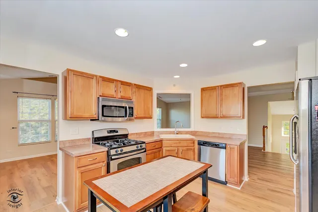 a kitchen with stainless steel appliances granite countertop a stove top oven a sink a dining table and chairs with wooden floor