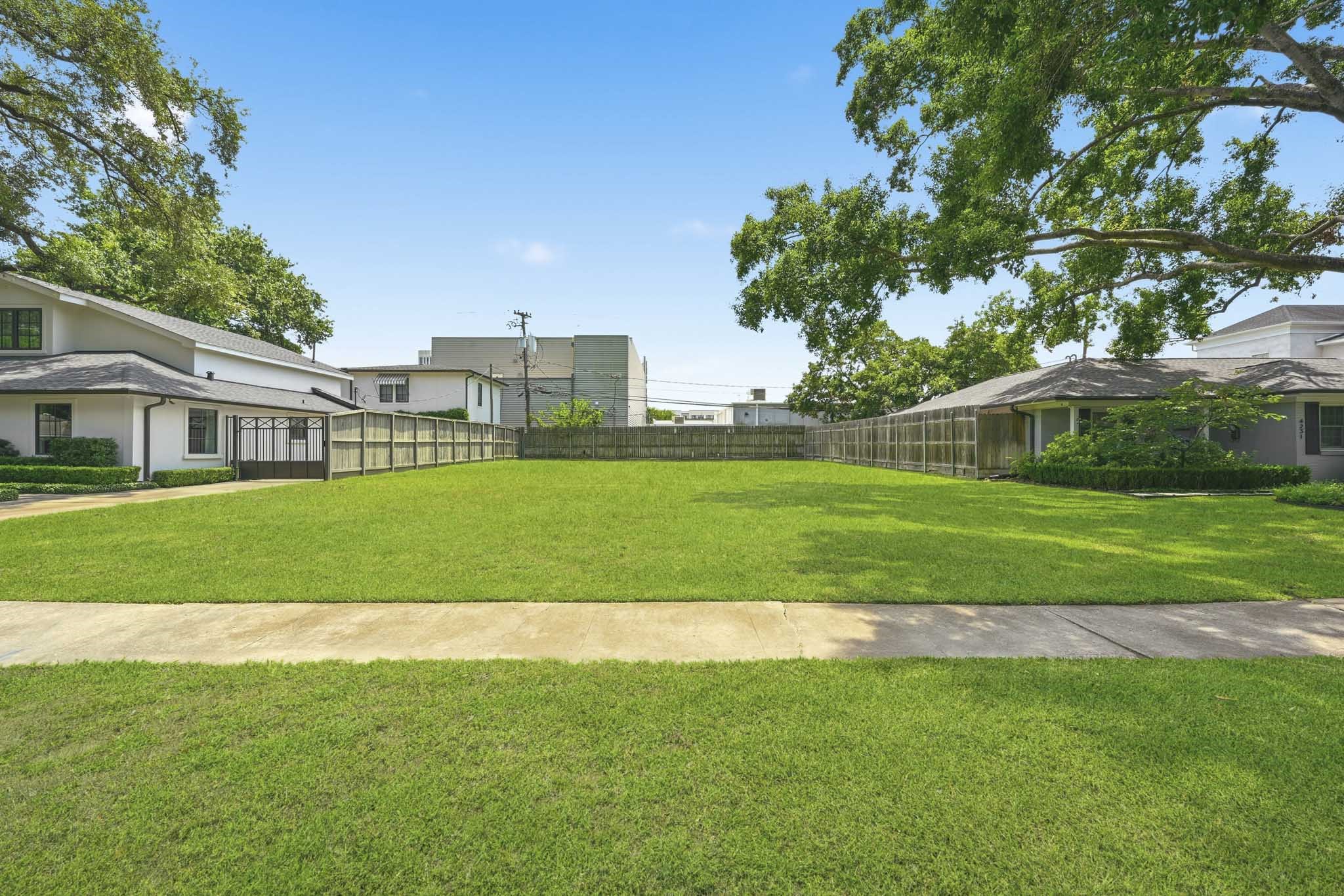 Spacious, well-maintained lawn with a fenced perimeter, surrounded by mature trees and adjacent homes. Ideal for outdoor activities and privacy.