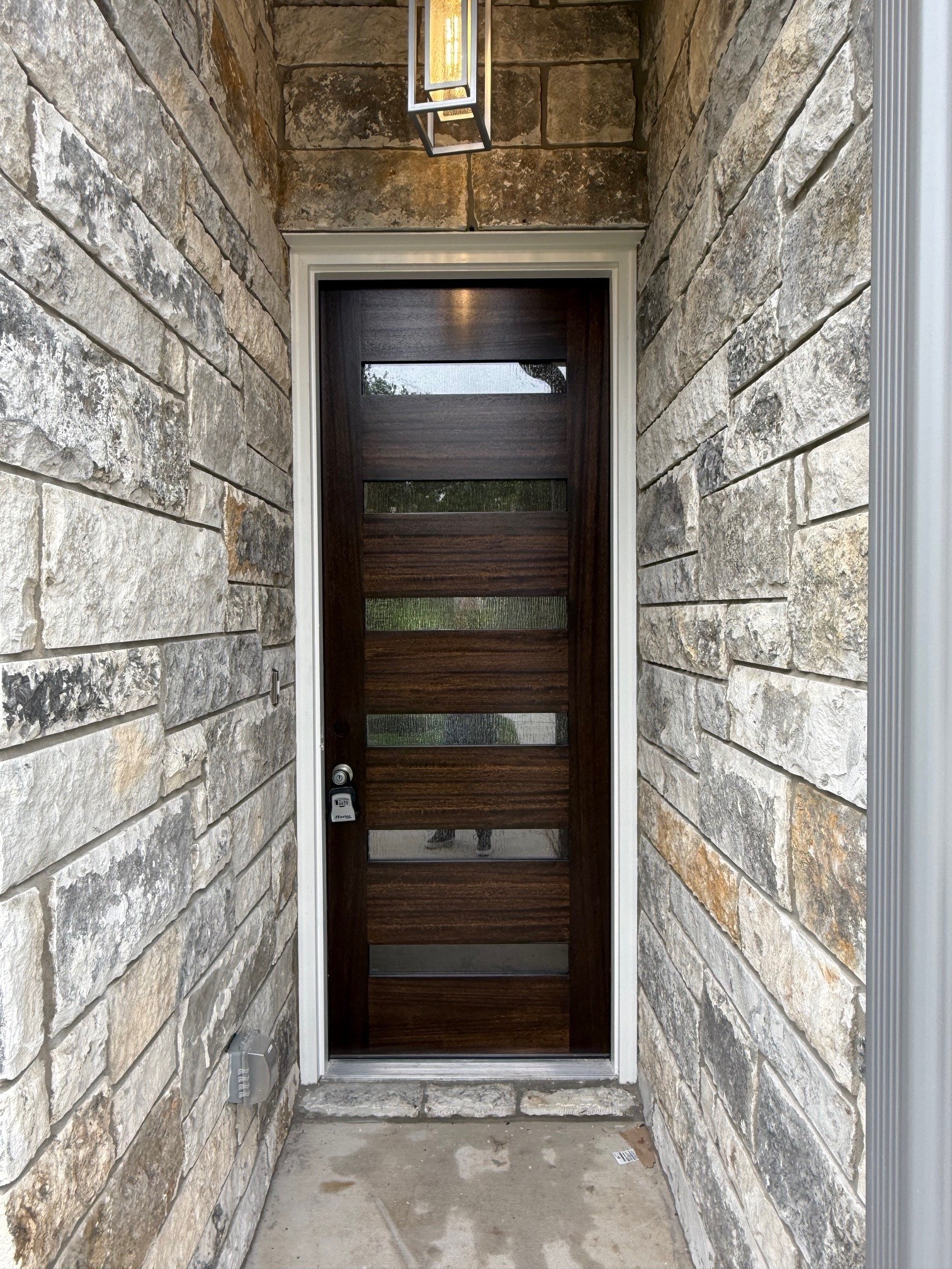 110 Firestone Place Meadowlakes, TX 78654 - Photo 3 of 18 Entryway featuring a stacked stone facade, a dark wood-finish door with horizontal glass panels, a white door frame, and a contemporary exterior light fixture