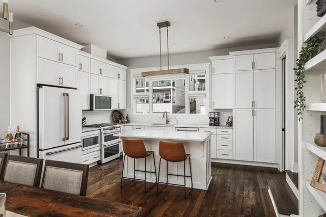 a kitchen with stainless steel appliances a dining table chairs a refrigerator and cabinets