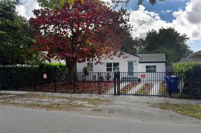 a view of a white house with a large tree and wooden fence