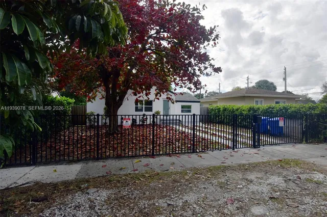 a view of a white house with a large tree and wooden fence