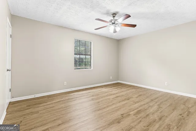 an empty room with wooden floor chandelier fan and windows