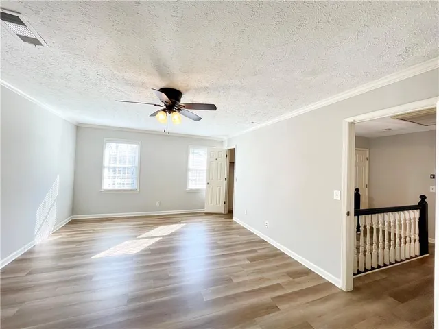 an empty room with wooden floor chandelier fan and windows