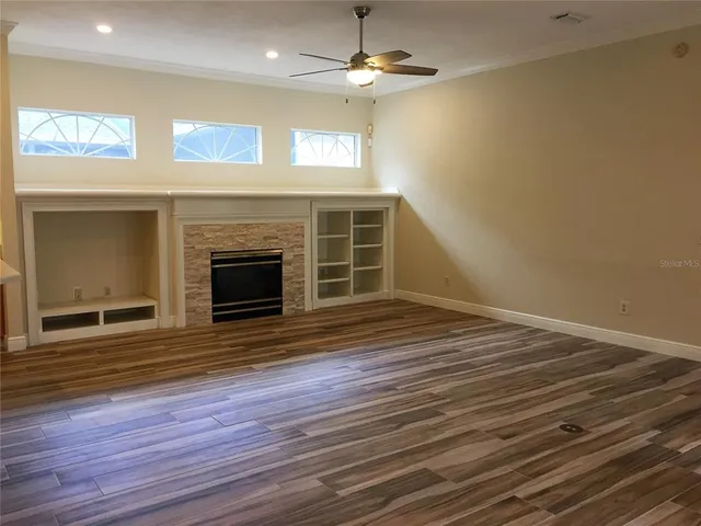 a view of an empty room with wooden floor fireplace and a window