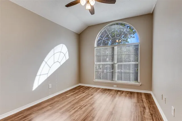 an empty room with wooden floor fan and windows