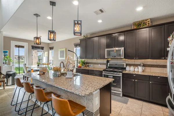 a kitchen with stainless steel appliances granite countertop a stove a sink dishwasher a refrigerator and a dining table with wooden floor