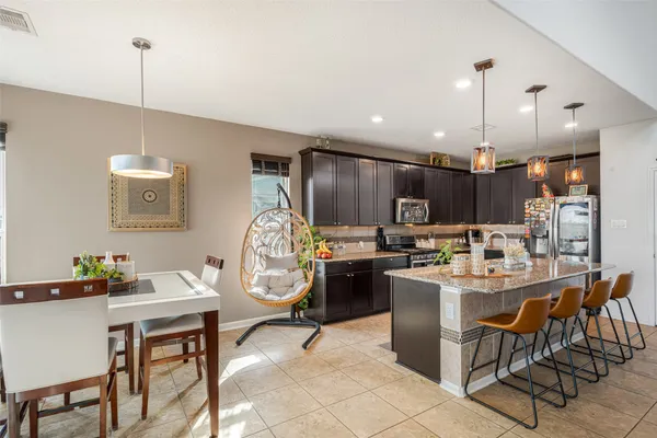 a kitchen with stainless steel appliances kitchen island granite countertop a dining table chairs and a refrigerator