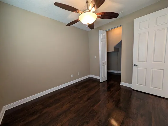 a view of an empty room with wooden floor and a ceiling fan