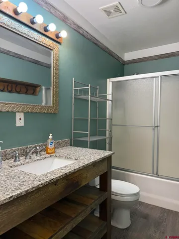 a bathroom with a granite countertop sink a toilet a mirror and shower