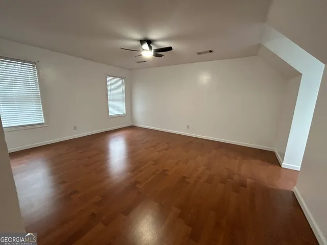 an empty room with wooden floor chandelier fan and windows