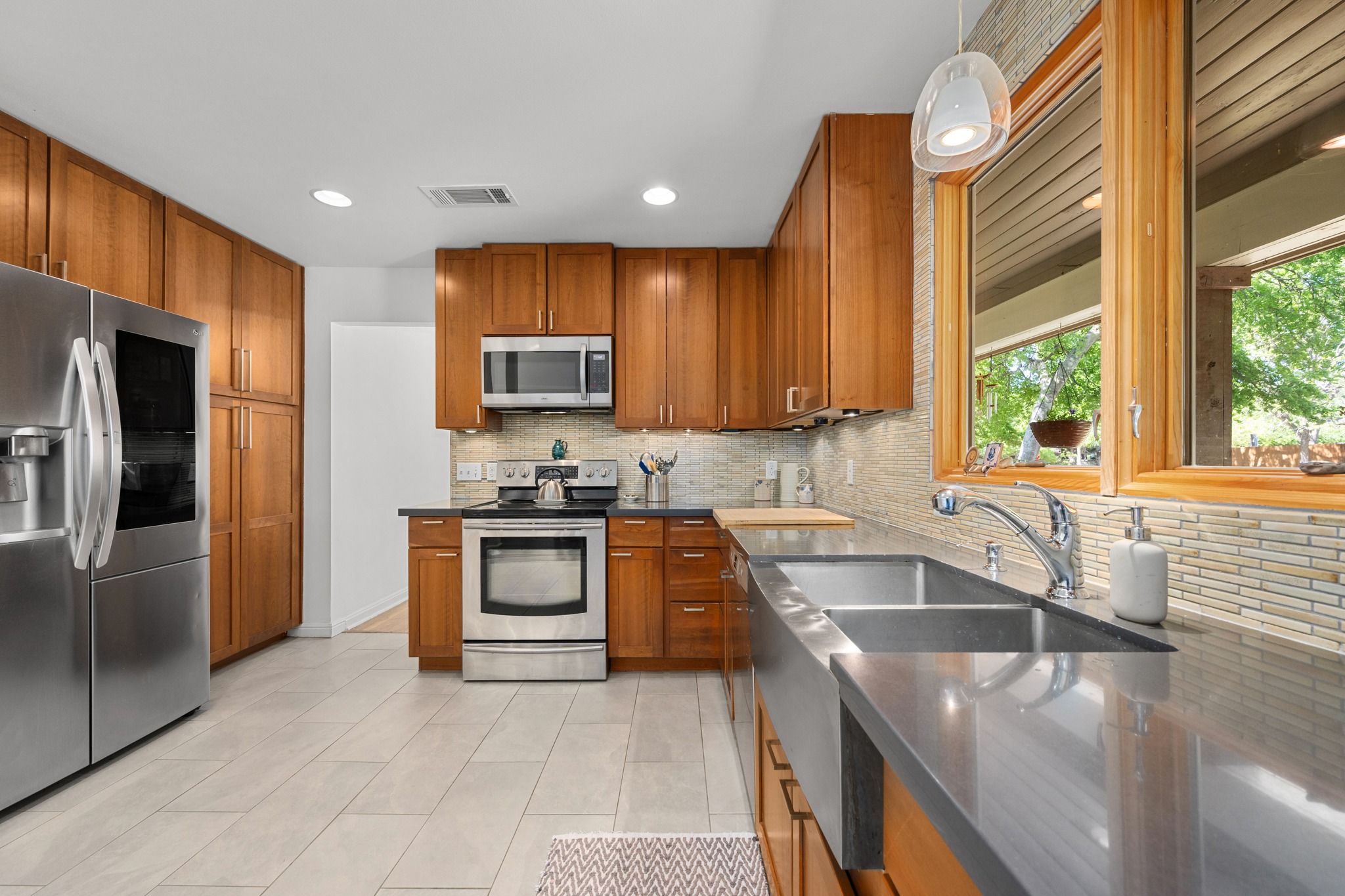 6103 Bull Creek Road Austin, TX 78757 - Photo 11 of 29 Kitchen with stainless steel appliances, wood finish cabinets, backsplash, dark stone counters, and hanging light fixtures