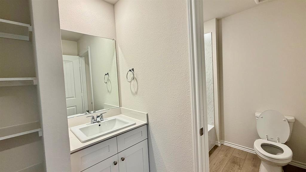 2003 Reveille Way Terrell, TX 75160 - Photo 4 of 25 Bathroom featuring a white vanity with an integrated sink, a rectangular wall-mounted mirror, and wood-finish flooring