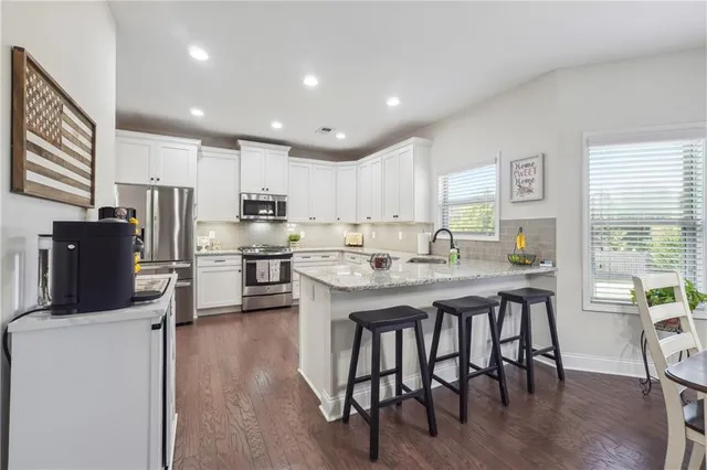 a kitchen with stainless steel appliances granite countertop a refrigerator a stove a sink a dining table and chairs with wooden floor