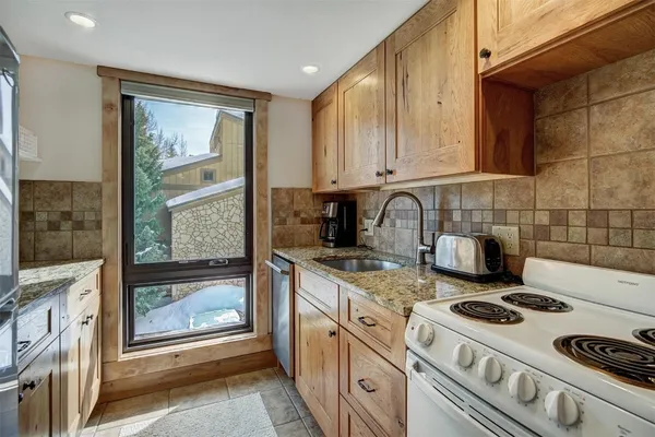 a kitchen with stainless steel appliances granite countertop a refrigerator a oven a sink with wooden cabinets and glass door