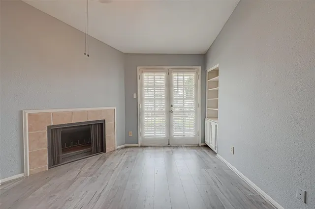 an empty room with wooden floor fireplace and windows