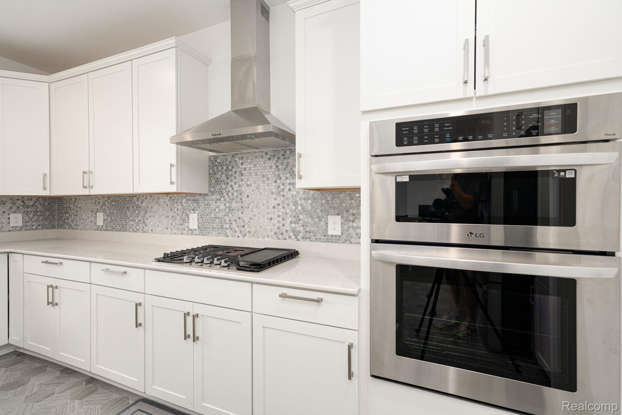 48904 Carnegie Way Macomb, MI 48042 - Photo 9 of 34 Gourmet kitchen featuring a stainless steel built-in oven and microwave, gas cooktop, white shaker cabinetry, light-toned countertops, and a patterned tile backsplash