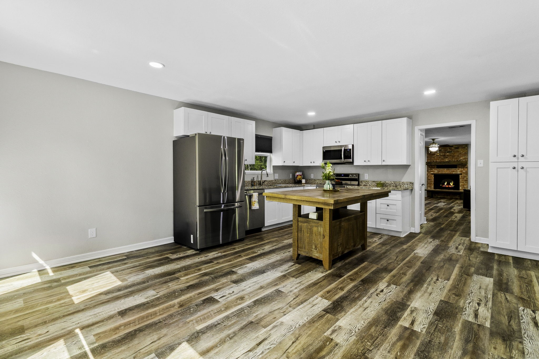 21 Red Oak Circle Point Blank, TX 77364 - Photo 7 of 32 Modern kitchen with stainless steel appliances, white cabinetry, and a large wooden island. The open layout features wood-look flooring and leads to a cozy living area with a brick fireplace.