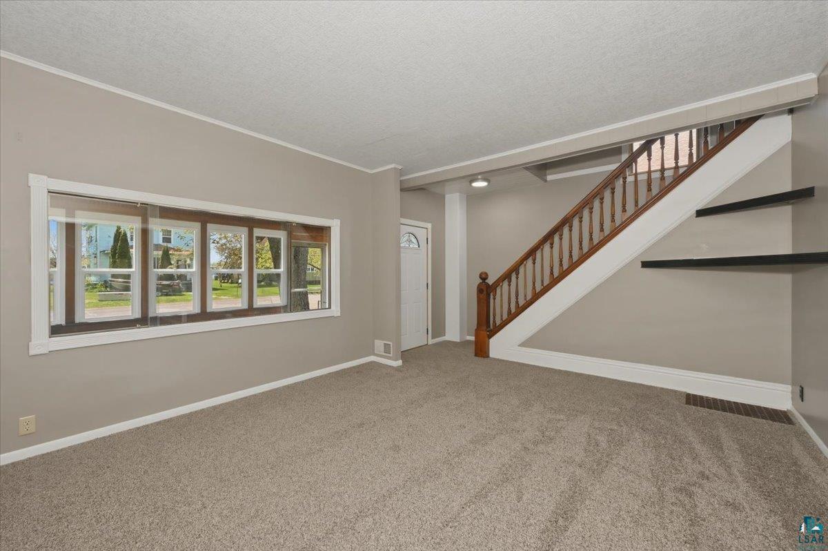 5319 East 3rd Street Superior, WI 54880 - Photo 20 of 33 Living area featuring new carpet, neutral wall tones, a panoramic window, a wood staircase with balusters, and built-in wall shelving
