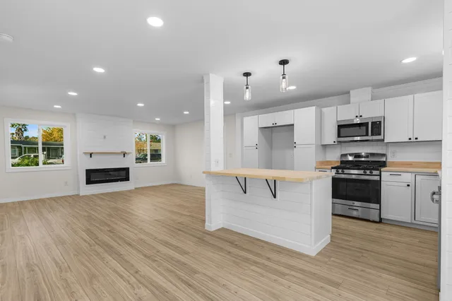 a kitchen with kitchen island granite countertop a stove a sink and white cabinets with wooden floor