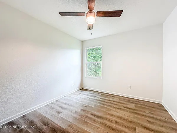 an empty room with wooden floor ceiling fan and windows