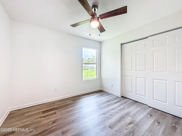 an empty room with wooden floor chandelier fan and windows