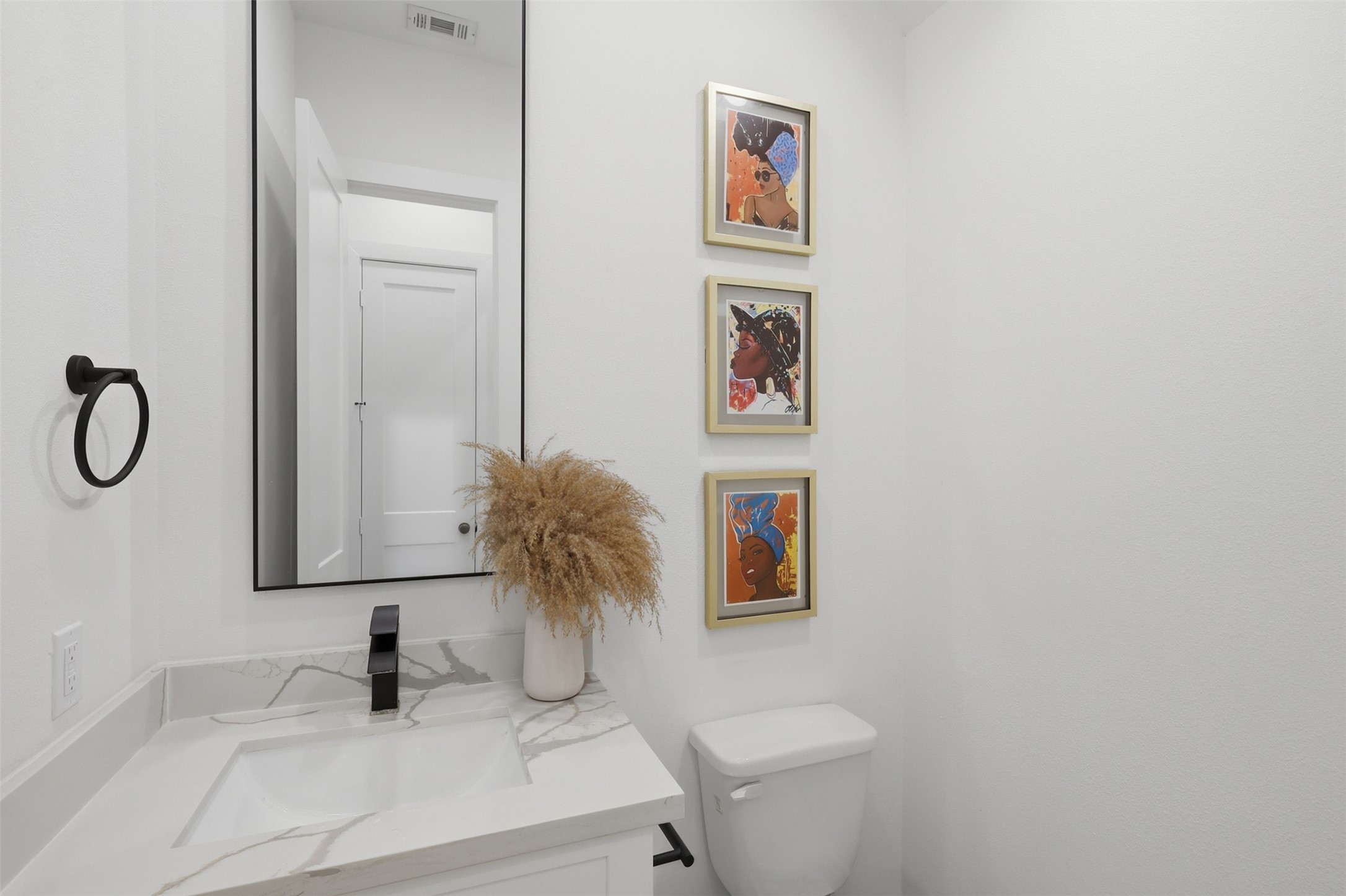 6833 Paris Street Houston, TX 77021 - Photo 10 of 23 This bathroom features a sleek, modern design with a marble countertop, a black faucet, and a large mirror. The white walls are adorned with vibrant artwork and there's a decorative vase with dried plants for an elegant touch.