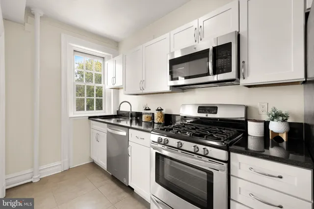 a kitchen with stainless steel appliances granite countertop grey cabinets a stove a sink and a microwave