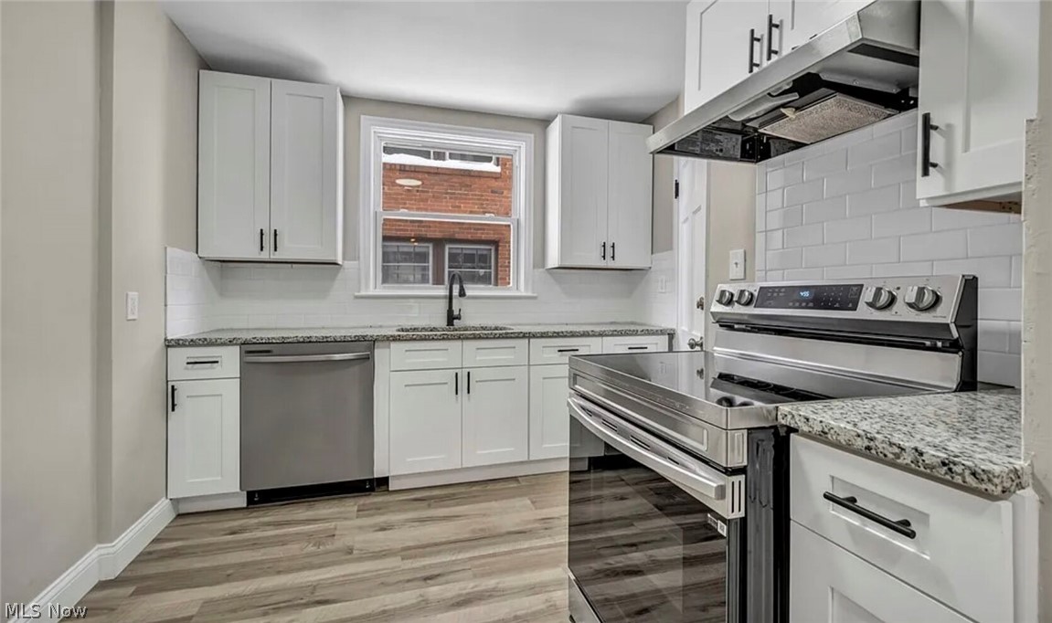 13614 Cedar Road, Unit DOWN University Heights, OH 44118 - Photo 9 of 16 Updated kitchen featuring white shaker cabinetry, stainless steel appliances, speckled countertops, a subway tile backsplash, and wood-finish flooring