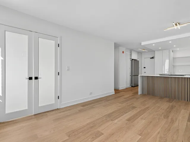 a view of an empty room with wooden floor and a bathroom