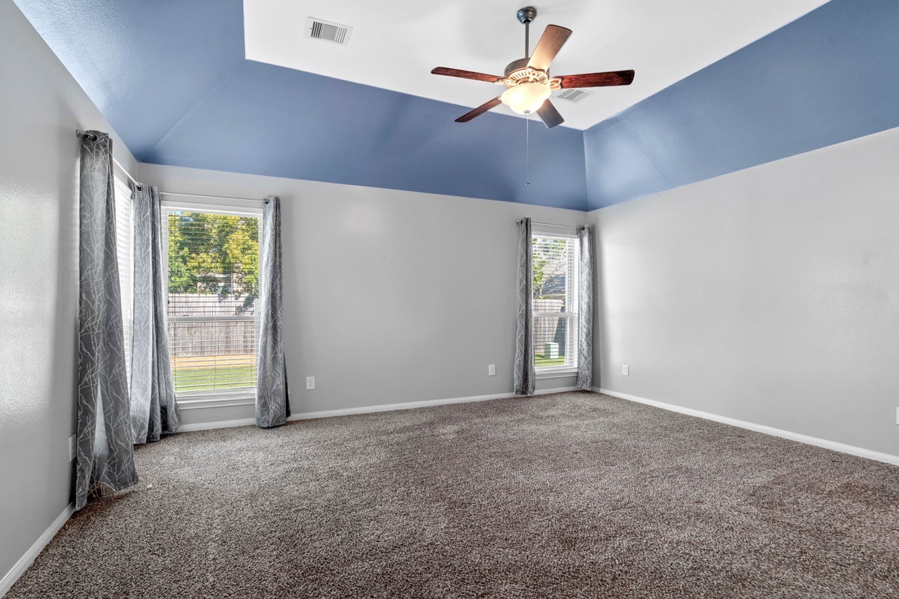 12126 Walden Road Montgomery, TX 77356 - Photo 19 of 50 Spacious primary bedroom featuring a high ceiling, large windows that fill the room with natural light, and plush carpet for added comfort. Neutral tones create a relaxing atmosphere, while ample wall space allows for flexible furniture placement. Views of the backyard enhance the serene feel of this inviting retreat.