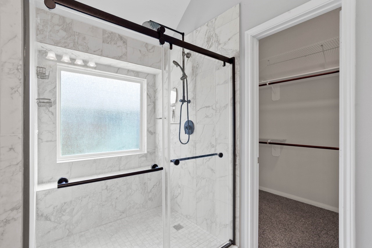 12126 Walden Road Montgomery, TX 77356 - Photo 22 of 50 Beautiful newly added walk-in shower featuring elegant marble-look tile, a frameless-style glass enclosure, and dual shower options including a rain shower head and handheld sprayer. The large, frosted window provides natural light while maintaining privacy, and sleek dark hardware adds a modern, high-end finish. Conveniently located next to the spacious walk-in closet for effortless daily living.