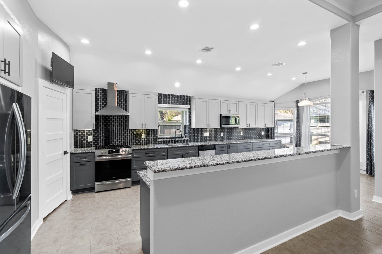 12126 Walden Road Montgomery, TX 77356 - Photo 25 of 50 This beautifully remodeled kitchen offers an expansive, open layout with stunning granite countertops, custom cabinetry, and a full-height designer backsplash that brings modern elegance to the space. A raised breakfast bar provides additional seating and connects seamlessly to the adjoining living and dining areas. Bright, LED recessed lighting and the large window over the sink fill the room with natural light, creating a warm and inviting atmosphere perfect for everyday living.