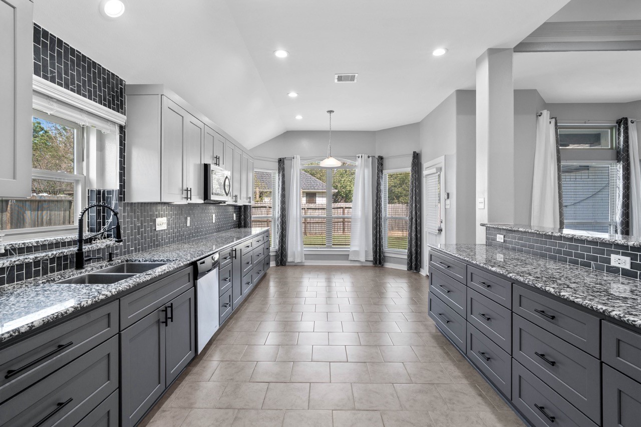 12126 Walden Road Montgomery, TX 77356 - Photo 27 of 50 Beautiful open-concept kitchen featuring expansive granite countertops, custom cabinetry, and a striking full-height tile backsplash that adds modern elegance throughout. The layout offers incredible workspace and storage, with dual walls of lower and upper cabinets, stainless steel appliances, and a deep undermount sink with updated fixtures. This kitchen seamlessly connects to the living spaces—perfect for entertaining, meal prep, or family gatherings.