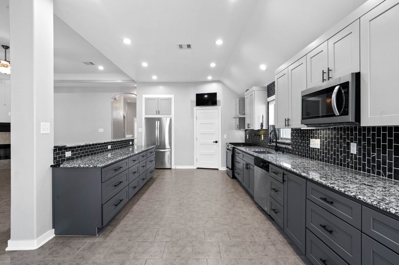 12126 Walden Road Montgomery, TX 77356 - Photo 30 of 50 Stunning remodeled kitchen featuring custom cabinetry, beautiful granite countertops, and a striking full-height tile backsplash that adds modern style and character. New stove, vent hood, microwave and refrigerator will convey with the home, along with the mounted TV. This kitchen also offers a spacious walk-in pantry for exceptional storage and organization. A perfect blend of function and design, ideal for everyday living and entertaining.